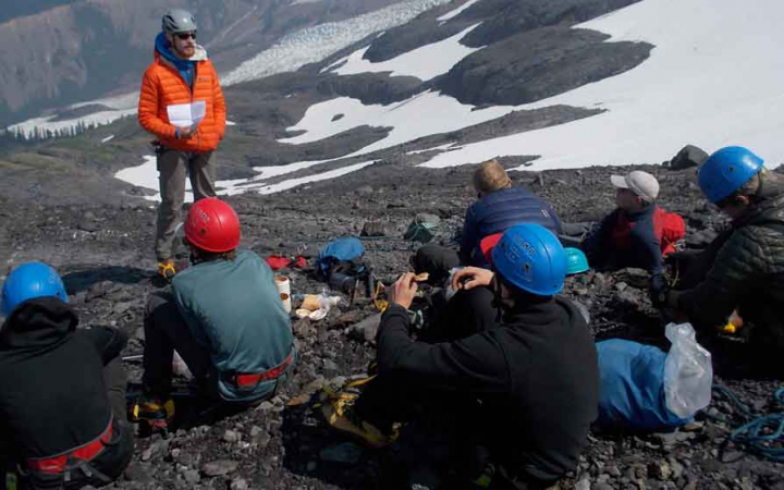 an instructor gives direction to a group of mountaineering students in a a rocky and snowy field